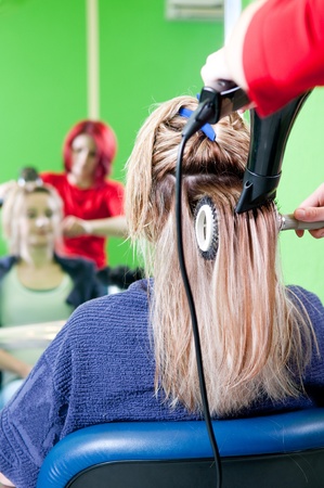 Close up of girl head in beauty salon while an hair stylist brush and dry her hairの写真素材