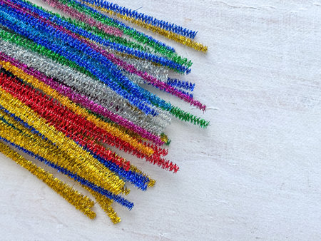 Colorful metallic pipe cleaners in gold, silver, red, blue, green, and pink shades placed diagonally...