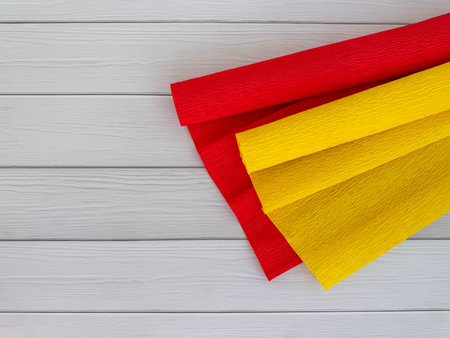Rolls of red and yellow crepe paper placed on light wooden background. Decorative craft materials used for DIY projects, gift wrapping, and creative decorations.の写真素材