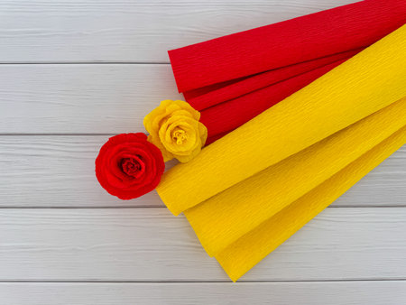 Decorative red and yellow crepe paper rolls with handmade paper flowers on light wooden background. Perfect for DIY projects, crafts.の写真素材