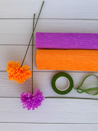 Handmade crepe paper flowers in purple and orange with matching rolls, floral stems, and green floral tape on wooden background. Perfect for DIY crafts, creative projects, party decor, and handmade gifts.の写真素材