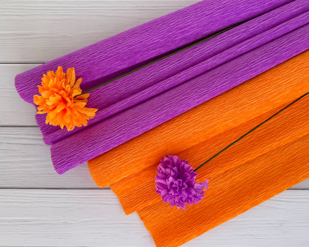 Handmade crepe paper flowers in bright orange and purple, styled as carnations, placed on matching crepe paper rolls. Ideal for crafting, party decorations, or festive DIY projects.の写真素材