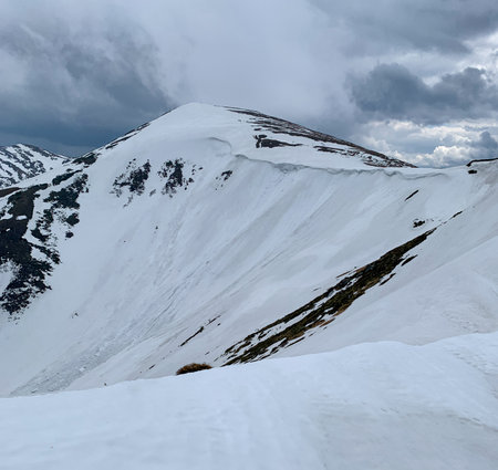 Massive snow cornice on Mount Shpytsi in the Carpathians. The steep white slopes and dramatic clouds emphasize the raw power of the mountains in spring.の写真素材