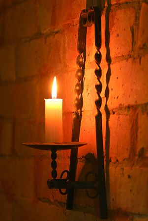 Candle in brass holder lighting wall of brick の写真素材