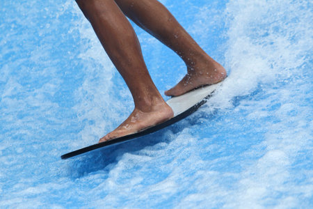 Close up a feet standing on surfboard when playing with water wavesの写真素材