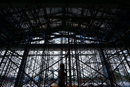 The shadow of a construction worker crosses a complex network of supports under a buildingの写真素材