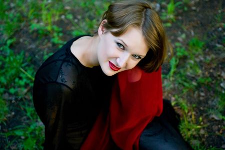 The young smiling women in black dress with red scarf against the green grassの写真素材