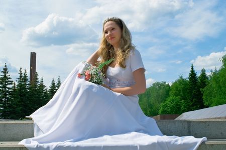 The happy bride in a white wedding dress with a flowers against blue skyの写真素材