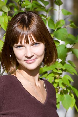 The young girl against green leaves in autumn parkの写真素材