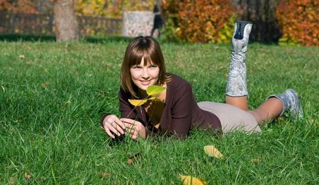 The young smiling girl on a green grass in autumn parkの写真素材