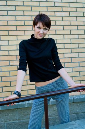 The young girl in black jumper and striped trousers at ladder against yellow brick wallの写真素材