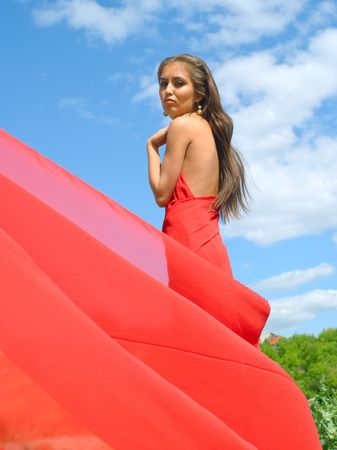 Beautiful girl in red dress against summer landscapeの写真素材