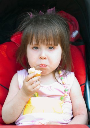 The little girl eats bread, sitting in a children's carriageの写真素材