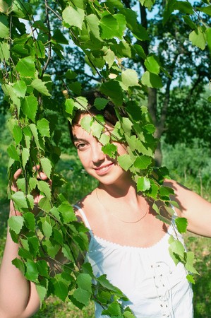 Beautiful girl in white dress and branch of the birch against summer landscapeの写真素材