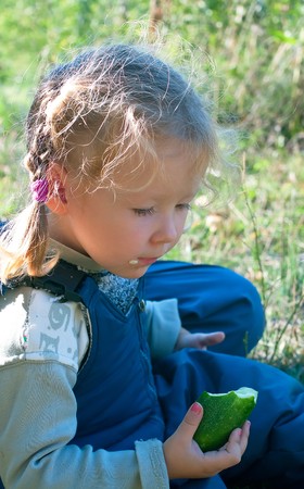 Portrait of the little girl with cucumber against summer landscape. Shallow DOF の写真素材