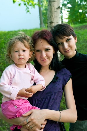Two young women with a little child on hands against summer nature. Shallow DOF 