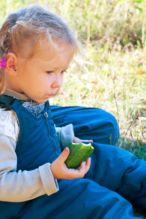 Portrait of the little girl with cucumber against summer landscape. Shallow DOF の写真素材