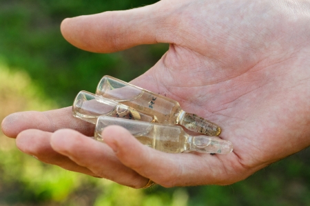 Three ampoules in a male hand on green background