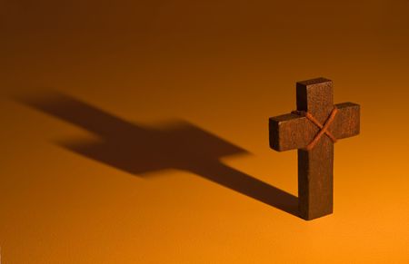 A moody image with a warm glow, of a wooden cross casting a deep shadow. Perfect for any religious and spiritual theme.の写真素材