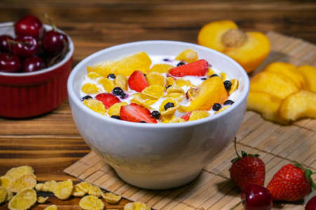 Dish with corn flakes, strawberry, cherry, peach and yogurt on the table.