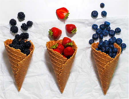 Waffle cone with delicious berries on white background