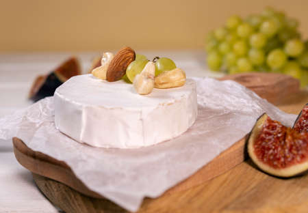 Camembert cheese on wooden board, branch of green grapes , slice of figs and nuts.