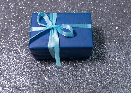 Blue box with golden ribbon on sparkling glitter paper backgound. Holiday background. Christmas concept. New year concept.の写真素材