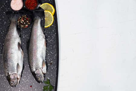 Fresh rainbow trouts on board on dark stone board with salt, pepper, lemon and rosemay ingredients. Tasty fishes preparing for lunch.の写真素材