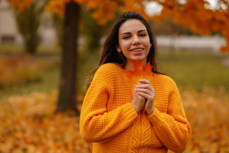 Beautiful European brunette with a autumn leave in her hands against the backdrop of an autumn park