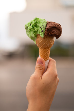 man s hand holding artisanal chocolate pistachio gelato in a cone,の写真素材