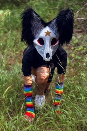 A quadrobing character on all fours peeks out from the tall grass in a leafy forest, creating a...