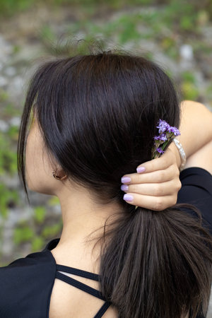 Back view close-up of a young woman holding her hair with hand and lilac flowers tucked in