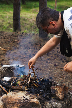 A man is lighting a campfire in the forest, creating a warm and cozy atmosphere in the wilderness....