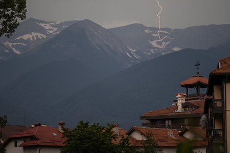 A powerful lightning bolt strikes a mountain in the distance, captured from the city view through...