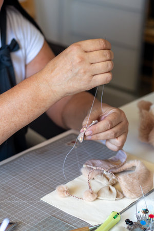 Close-up of a person's hands meticulously sewing details onto a plush toy part with a needle and thread, showing the craftsmanship involved in handmade creations.の写真素材