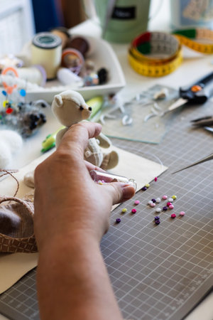 Pours colorful buttons from bottle onto mat, beside a mini teddy bear. Captures the joy of intricate creative handicraft.の写真素材