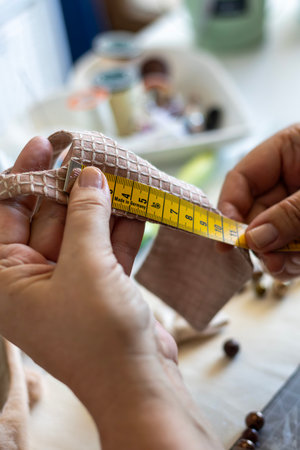 A close-up view of two hands carefully measuring a piece of patterned fabric with a yellow tape measure. This image depicts the precision and detail involved in crafting or sewing projects.の写真素材