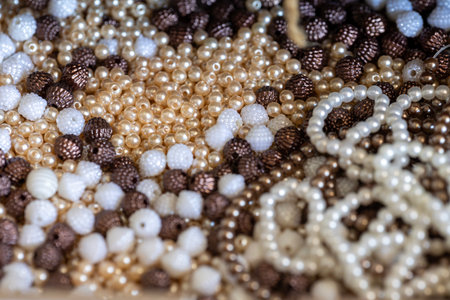 A close-up of various crafting beads in shades of white, cream, gold, and textured brown, ideal for jewelry making, fashion accessories, and creative DIY projects.の写真素材