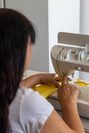 A person's hands guide yellow fabric through a sewing machine, engaged in a creative project. This...