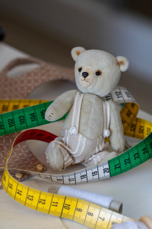 This adorable, soft teddy bear sits amidst colorful measuring tapes, fabric, and thread, creating a charming scene of handicraft and meticulous creation.の写真素材