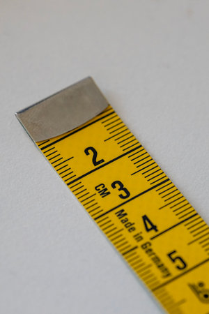 Close-up detail of a bright yellow fabric tape measure with a metal end, showing CM markings and...