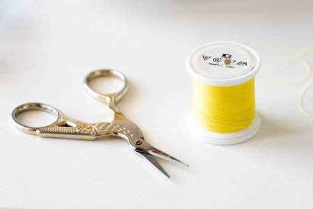 A bright yellow spool of polyester thread sits beside a pair of elegant, antique-style silver...