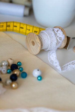 A close-up of crafting supplies including a wooden spool of white lace, colorful beads, and a yellow...