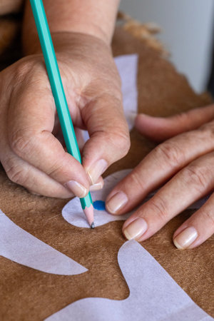 Close-up of hands carefully tracing a white craft pattern onto a brown fabric or felt material using a pencil. This image evokes the joy of DIY projects, creative hobbies, and handmade artistry.の写真素材