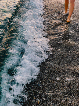 A person is walking along the beach, feeling the gentle waves lap at their feetの写真素材