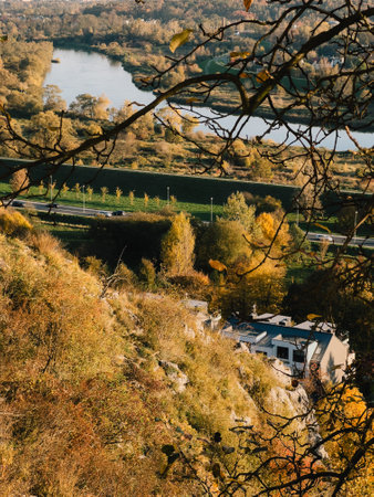 Autumn river valley with winding waterway, vibrant fall colors, roadside scenery, and hidden buildings surrounded by golden leaved treesの写真素材