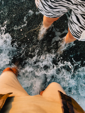 Barefoot tourists splashing through gentle ocean waves, feeling warm sand beneath feet during sunny summer beach vacation, enjoying relaxed seaside momentの写真素材