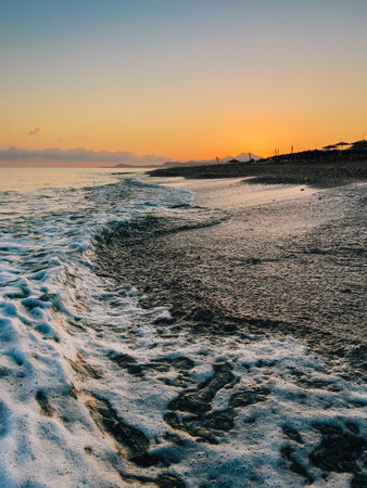Sunset waves gently caressing golden shoreline, warm orange and pink tones softening twilight horizon with peaceful coastal serenityの写真素材