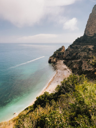 Motorboat sailing in sea near beach with its characteristic rock formations and crystalline waters. Serene beach scene beautifully showcasing rocky cliffs and clear watersの写真素材