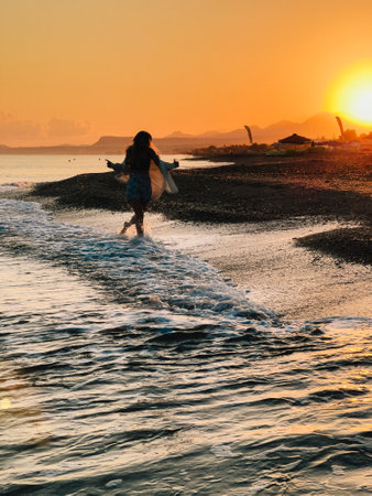 Young woman running on beach at sunset enjoying freedom and happiness. Young woman is walking on beach at sunset, enjoying freedom and happiness of the moment, with waves gently lapping at her feetの写真素材